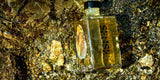 Obsidian Glow Flasche im goldenen Wasser über Steinen — Set the Scene